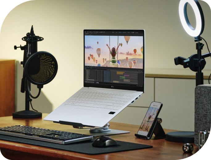 The LG gram is on a desk with a microphone and ring light, with a video editing screen, showcasing high performance despite its light weight.