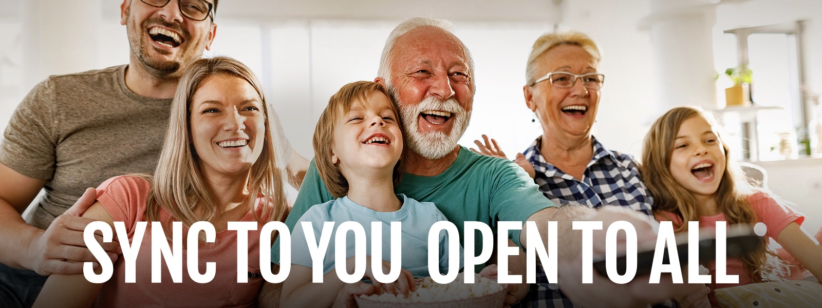 A family sits laughing while the grandfather points the remote outward. 