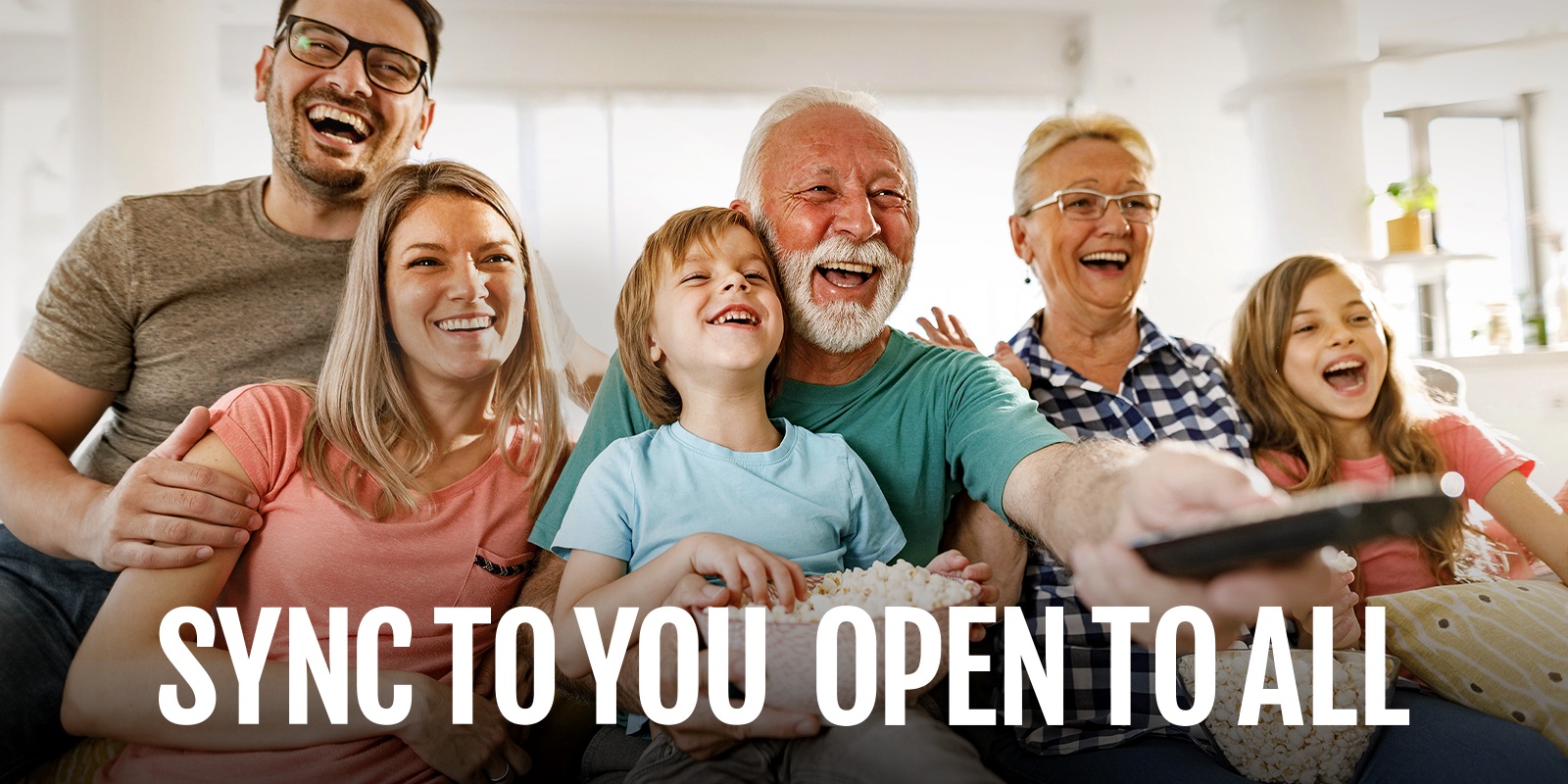 A family sits laughing while the grandfather points the remote outward. 