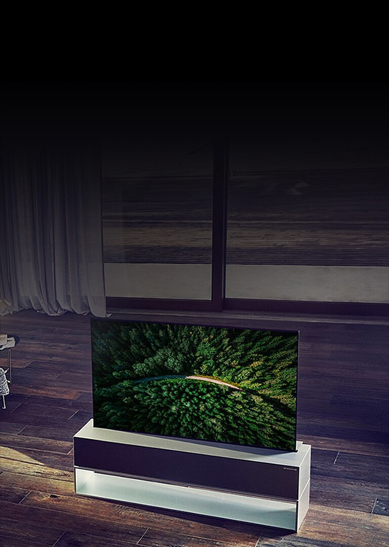 Le téléviseur OLED enroulable LG SIGNATURE est placé sur le parquet du salon de luxe et un homme regarde la télévision.