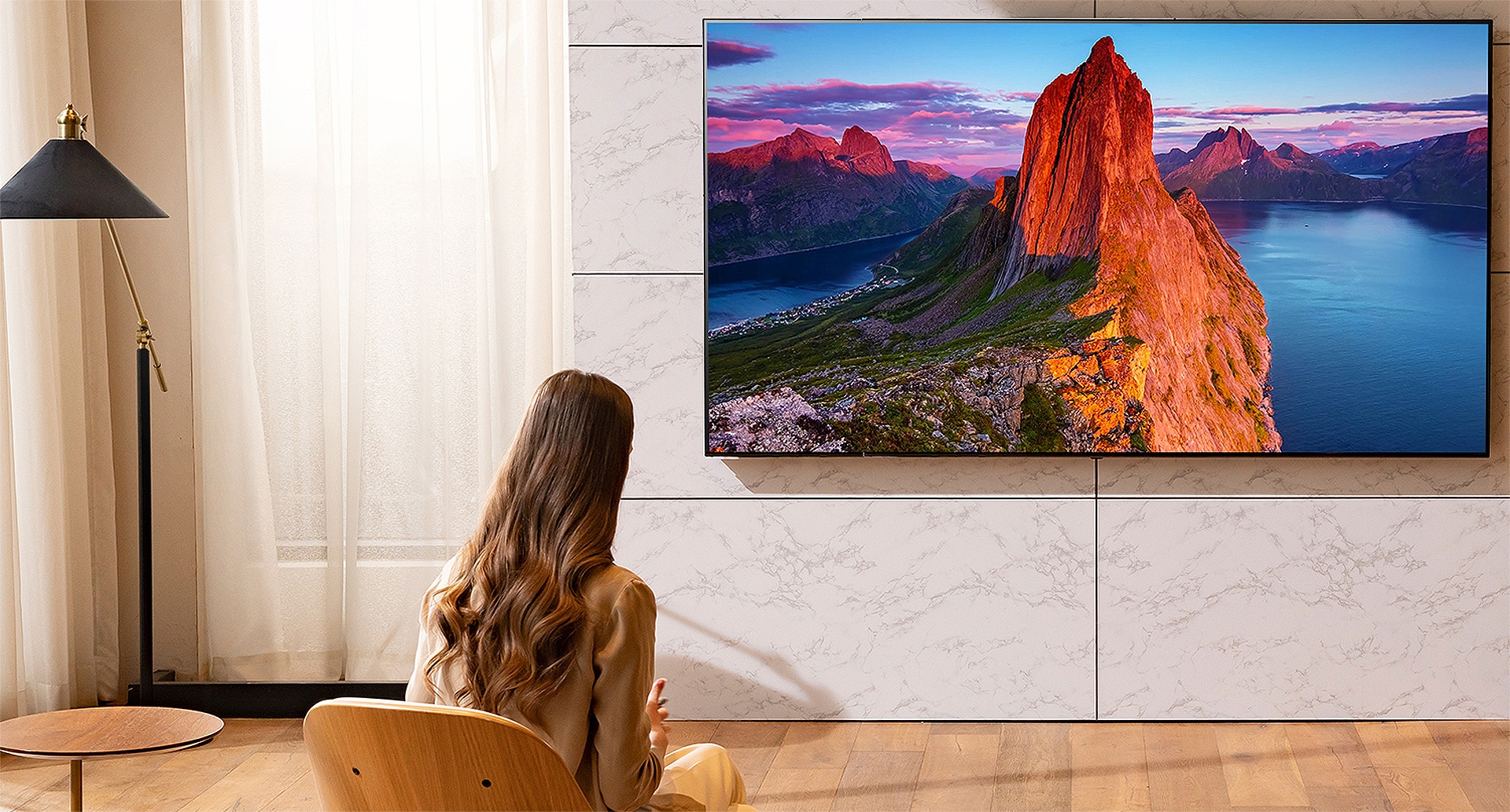 Une femme regarde la télévision dans un salon. L’écran du téléviseur affiche un paysage.