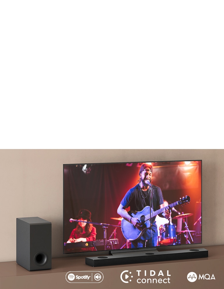 Телевизор LG е поставен на кафяв рафт, саундбар S90QY на LG е поставен пред телевизора. Субуфер е поставен от лявата страна на телевизора. Телевизор показва концертна сцена. В горния ляв ъгъл е показано обозначението НОВО.
