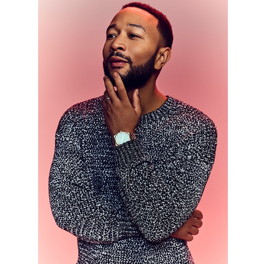 Bild von John Legend, der sein Kinn vor einem roten Hintergrund berührt.