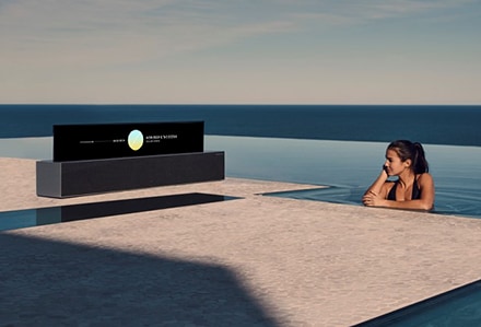 Eine Frau in einem Pool hört dem Programm im Line View-Modus eines aufrollbaren OLED TV R zu.