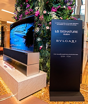 Ein Schild über die Kollektion von LG SIGNATURE und BVLGARI befindet sich neben einem aufrollbaren OLED TV R. 