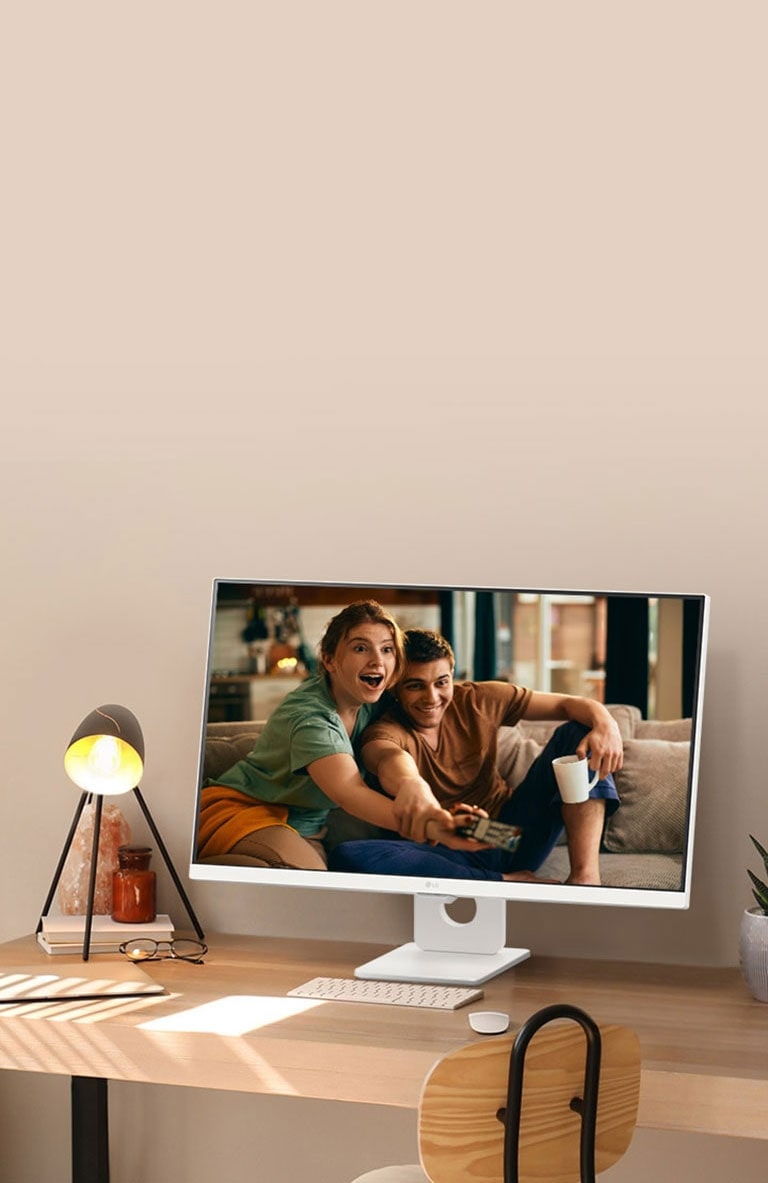 Sur un bureau à côté d’une fenêtre ensoleillée, un moniteur intelligent affiche un film sur son écran. À côté du moniteur se trouvent une lampe et une plante en pot. Sur le bureau se trouvent un clavier et une souris.