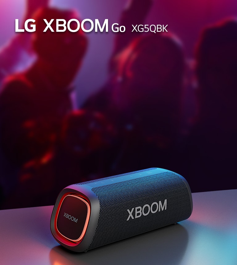 LG XBOOM Go XG5 放置在金属桌子上，橙色灯亮起。人们在桌子后面享受音乐。