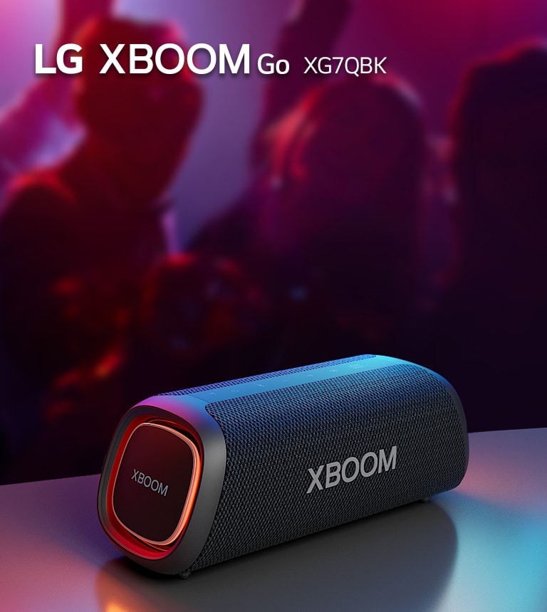 LG XBOOM Go XG7 放置在金属桌子上，橙色灯亮起。人们在桌子后面享受音乐。