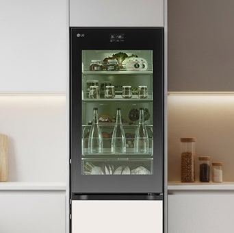 Geladeira LG alta com porta de vidro transparente em uma cozinha minimalista. O interior está iluminado com luz verde, mostrando claramente mantimentos e bebidas frescos armazenados.