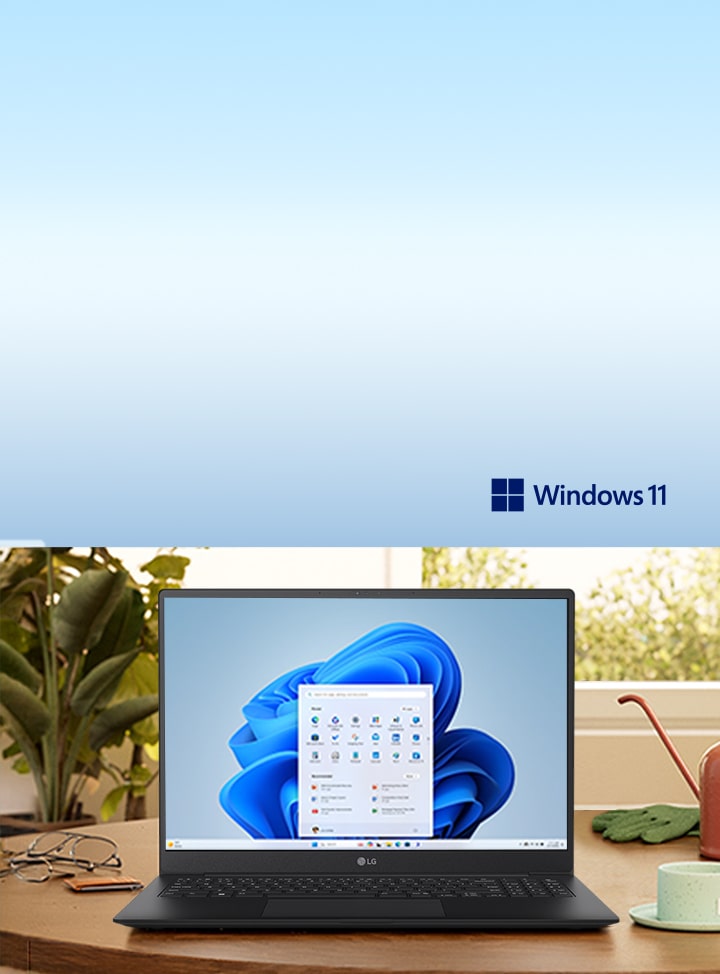 Esta imagen muestra un ordenador portátil con Windows 11 sobre un escritorio de madera, rodeado de plantas y una lámpara, lo que evoca un espacio de trabajo sereno.