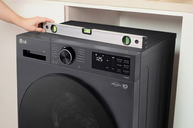 Black LG washing machine with a spirit level placed on top to check that the appliance is horizontally aligned.