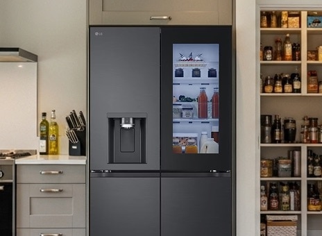 LG matte black Multi-Door fridge freezer with InstaView Door-in-Door open, showing fresh food storage. To the right, pantry shelves are filled with groceries.