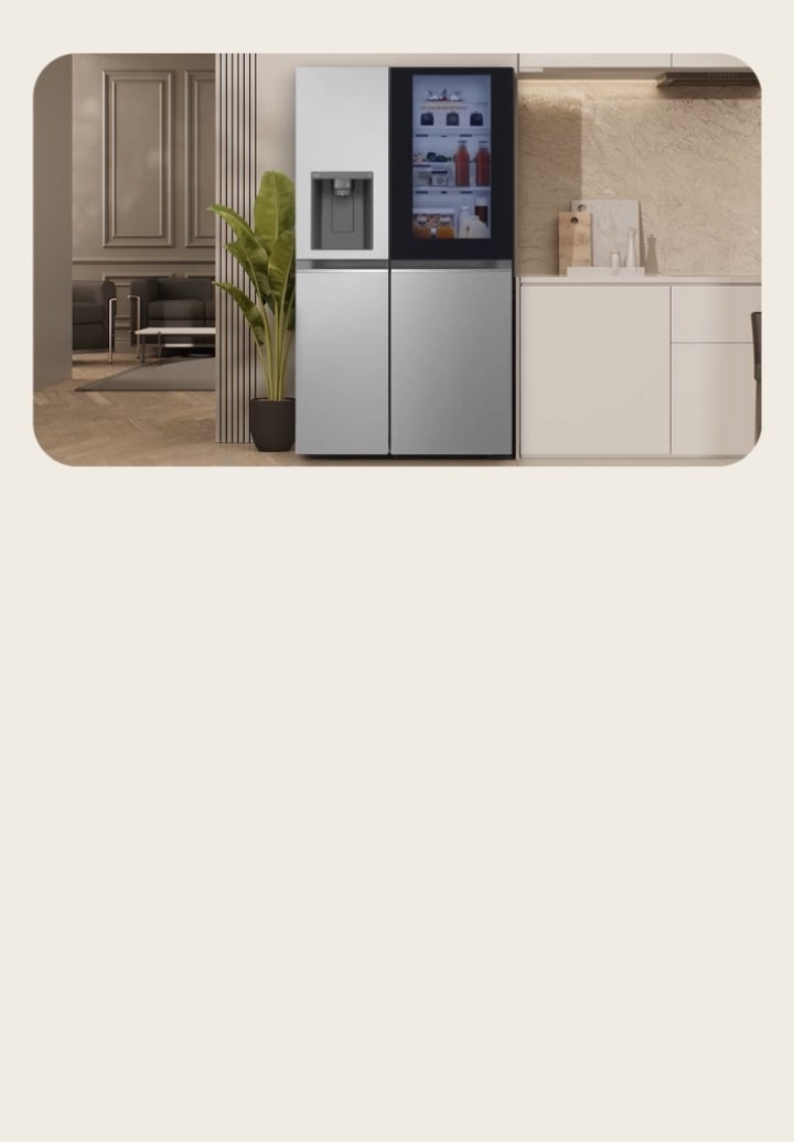 LG silver American style fridge freezer with InstaView and water dispenser placed at the center. A large plant is on the left and a modern kitchen is visible on the right.