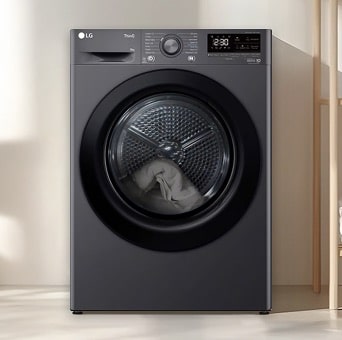 LG black tumble dryer installed under a counter in a laundry area. The transparent door shows laundry inside, clearly visible through the front of the machine.