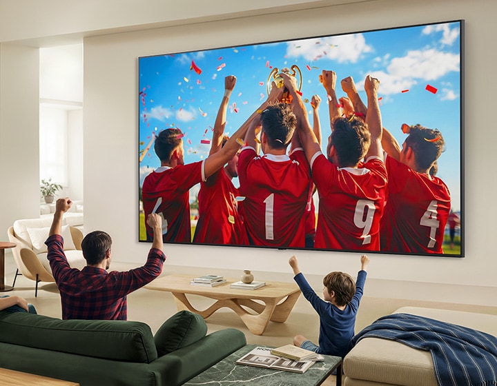 LG QNED evo AI QNED85 Mini LED Ultra Big TV is wall-mounted in a living room, displaying a sports victory celebration with vivid colours and refined picture quality across the wide screen as a family seated on sofas cheers together.