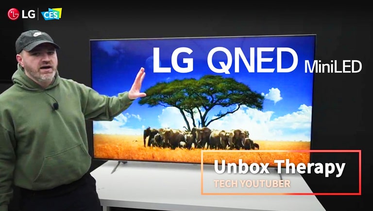 Der Tech-YouTuber Unbox Therapy steht vor einem LG QNED Mini LED TV. Der Bildschirm zeigt eine Elefantenherde, die um einen einzelnen Baum herumsteht.