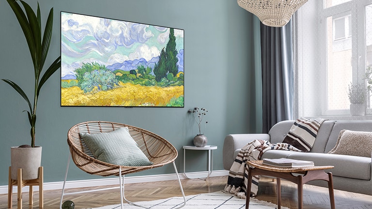 Ein Fernseher, der Kunst anzeigt, hängt an der grünen Wand eines Wohnzimmers, in dem sich außerdem ein Sessel, ein Sofa und ein Blumentopf befinden.