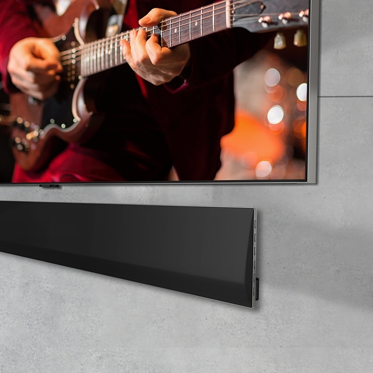 Ant sienos sumontuoto LG OLED TV ir LG Soundbar apatinės dalies vaizdas iš arti, kampu.