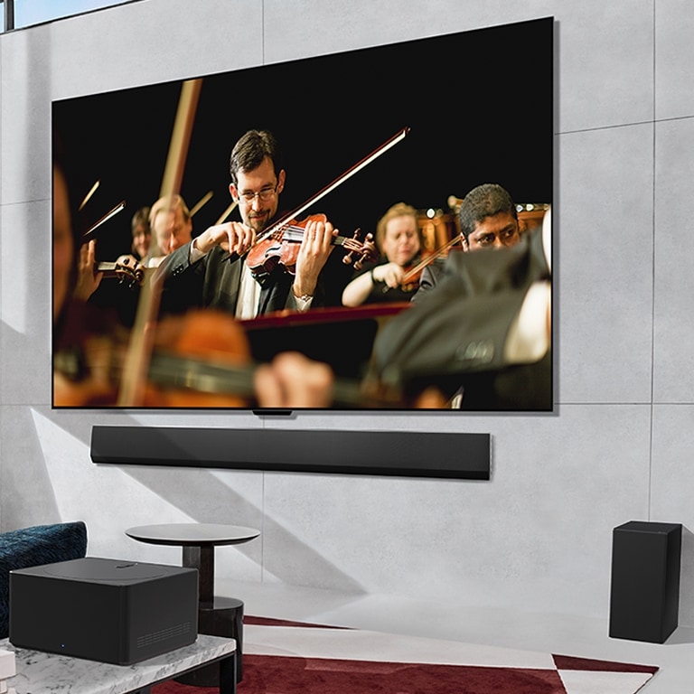 LG OLED TV, kurio ekrane groja orkestras, plokščiai pritvirtintas prie sienos, o priešais pastatytas „Zero Connect Box“.