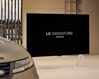 LG SIGNATURE OLED M4 ant stendo „Range Rover House“ prie „Range Rover Sport SV“, o paveikslėlio apačioje – atkūrimo mygtukas.