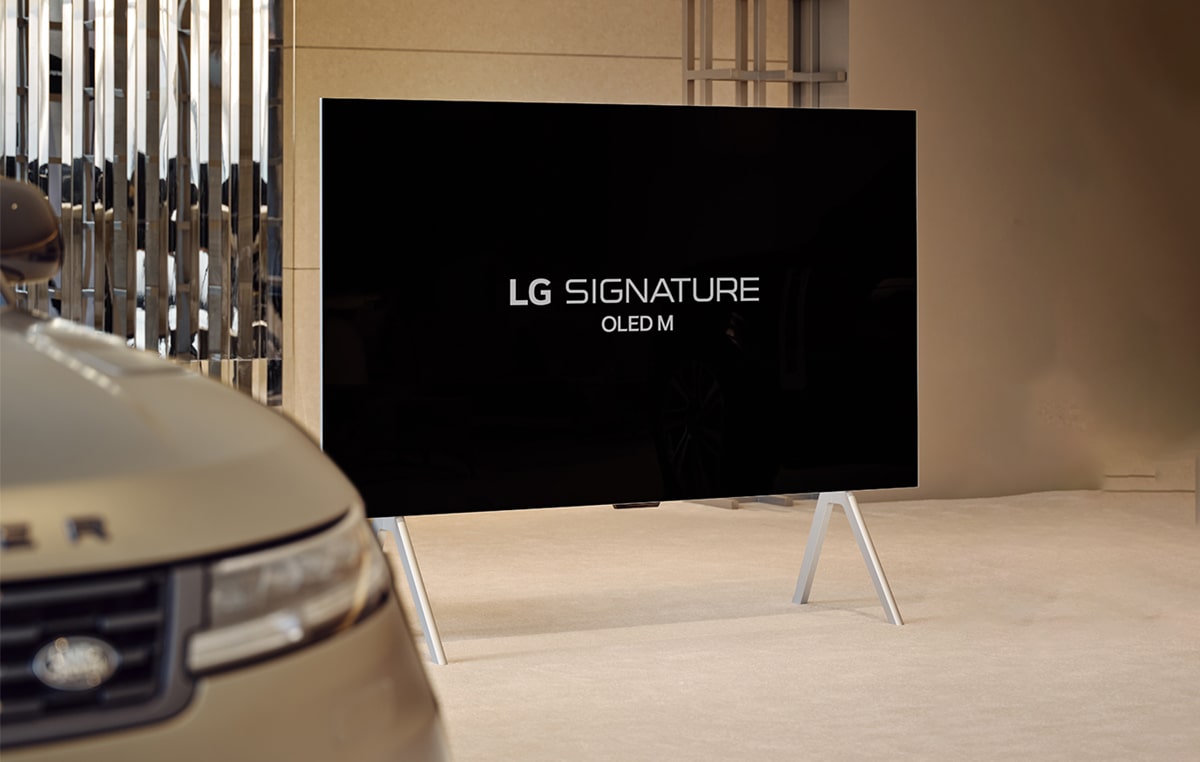 LG SIGNATURE OLED M4 auf einem Standfuß im Range Rover House neben dem Range Rover Sport SV, mit einer Wiedergabe-Schaltfläche am unteren Rand des Bildes.