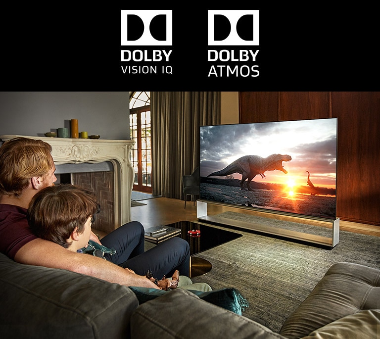 Das Zeichen von DOLBY VISION IQ / Das Zeichen von DOLBY ATMOS, Vater und Sohn schauen einen Dinosaurier-Dokumentarfilm auf einem Großbildfernseher