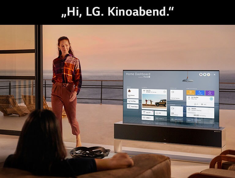 Ein Mann nimmt eine Verbesserung der Einstellungen für Kinofilme über das Home Dashboard des Fernsehers im Wohnzimmer vor, das zu einer Terrasse am Meer führt.