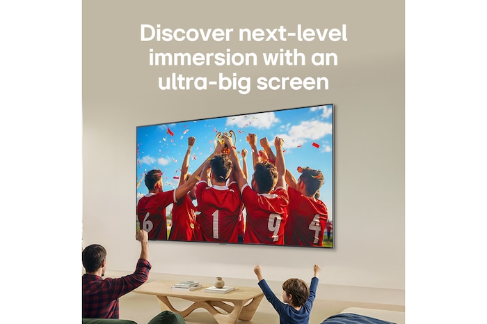 LG QNED AI QNED70 Mini LED Ultra Big TV is wall-mounted in a bright living room, showing an intense soccer moment with vivid colors and refined picture quality across a wide screen, as a family seated on sofas cheers together.
