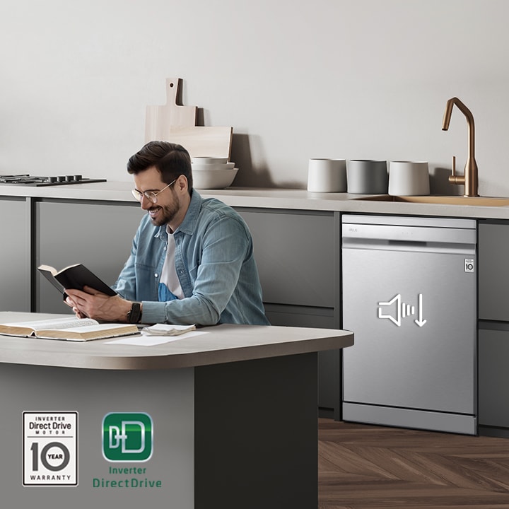 A man reading a book at the kitchen island while the LG free-standing Dishwasher is running in the background.