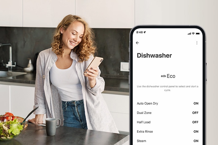 A woman is setting cleaning cycle preferences using the LG ThinQ app in the kitchen.