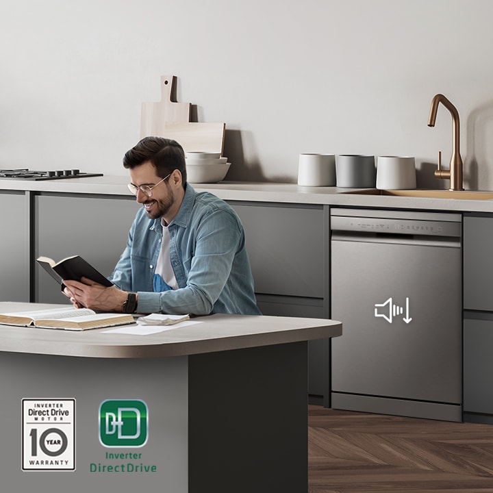 A man reading a book at the kitchen island while the LG free-standing Dishwasher is running in the background.
