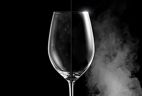 A wine glass with water spots on one side, and clear and pristine on the other after steam washing.