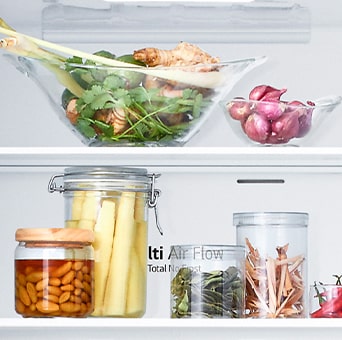 Close up view of lg bottom freezer refrigerator shelf with various fresh herbs, vegetables, and preserved foods in glass containers.	