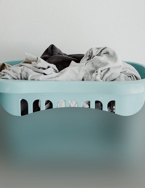 A light blue laundry basket filled with assorted clothes against a plain white background.