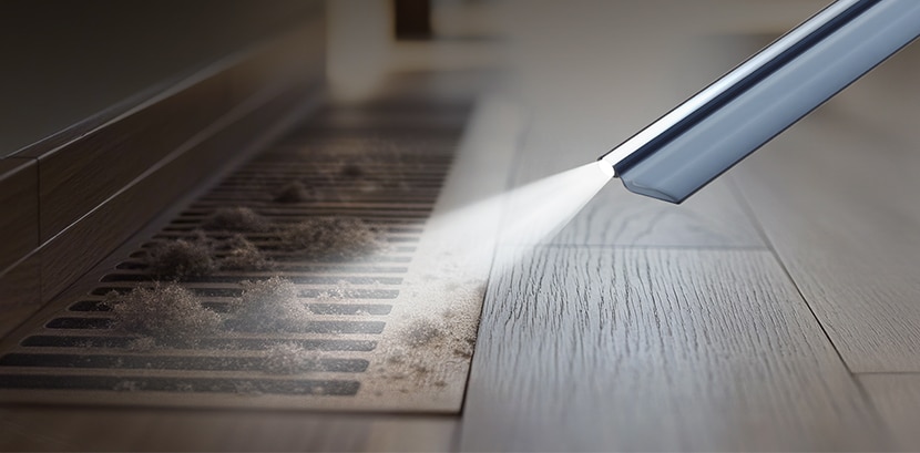 LED crevice tool cleaning dust from a floor vent in low light.