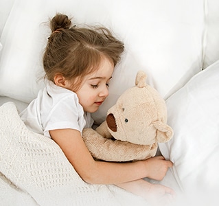 A little girl is lying in bed with a Teddy Bear in her arms	