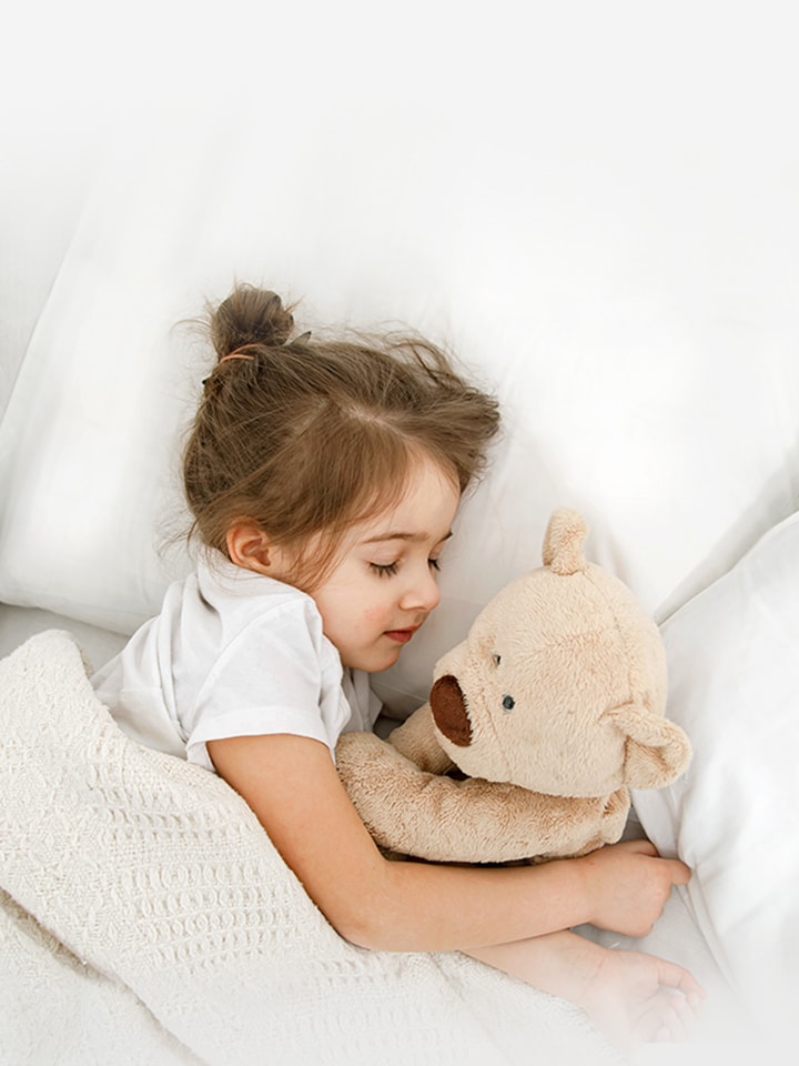 A little girl is lying in bed with a Teddy Bear in her arms	