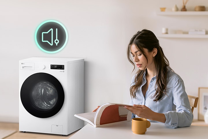 The woman is sitting at a table reading a book and showing icons and washing machines that have less noise next to her