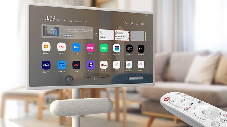 The LG XT7S speaker is attached on the LG StanbyME in the living room. The screen displays the home screen. On the bottom-right corner of the image, LG magic remote is shown.