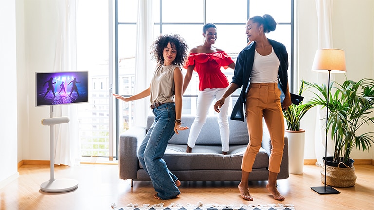 The LG StanbyME is placed in the living room with the XT7S speaker attached. People enjoy the music with the screen and speaker combo.