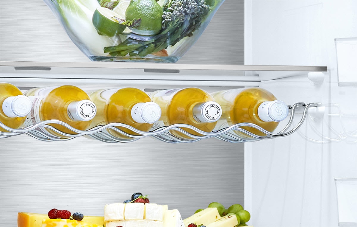 Refrigerator interior with white wine bottles, fresh green salad in a bowl, and sliced cheese with fruits.