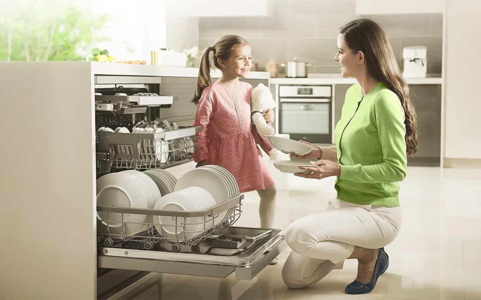 Mother and daughter happily unloading dishes from a dishwasher in a bright and spacious kitchen, making cleaning a family activity