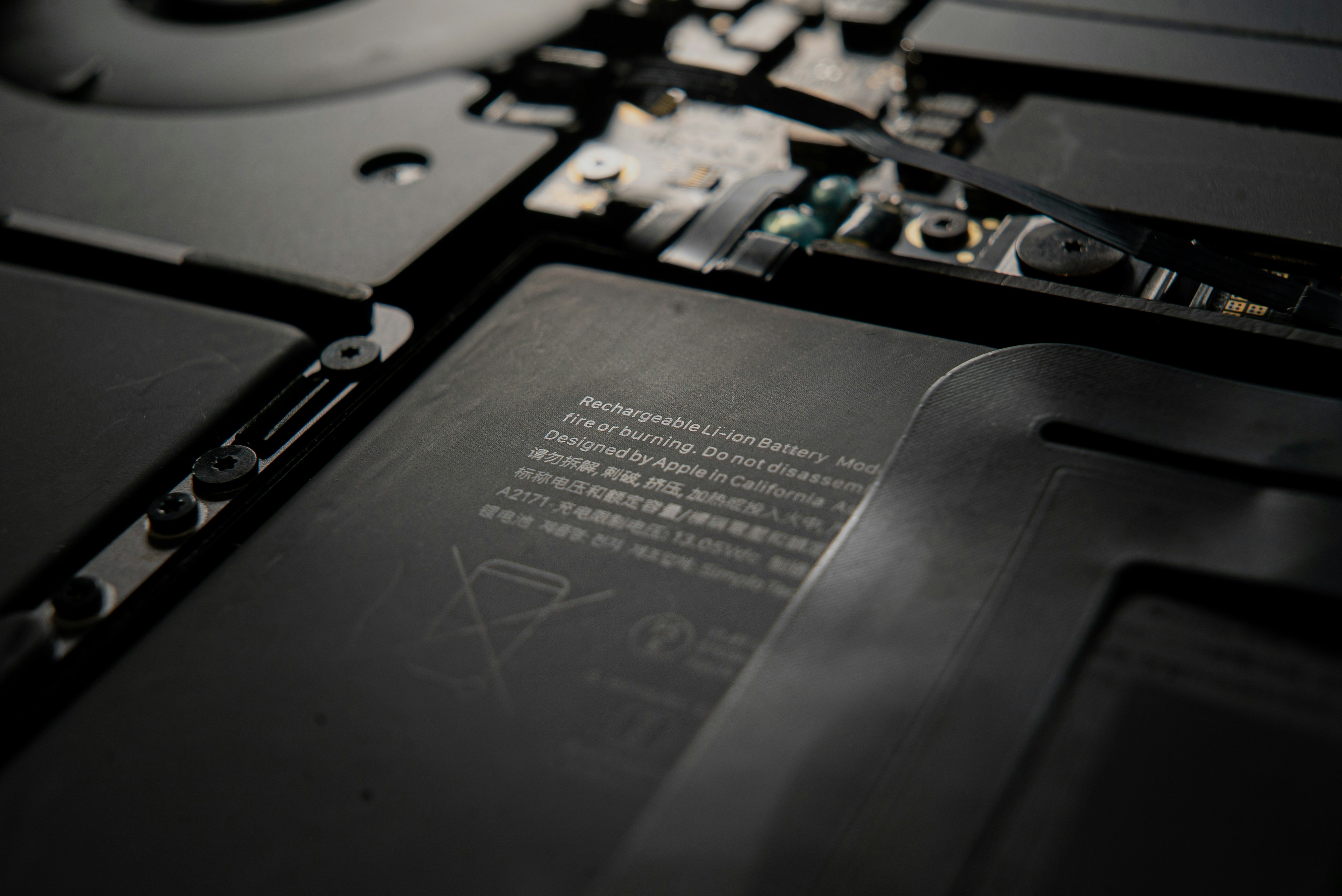 Close-up view of a rechargeable lithium-ion battery inside a laptop, emphasizing text warnings and disposal icons.