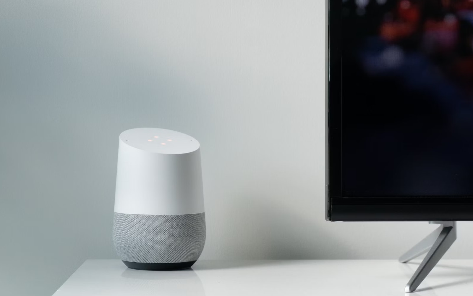 Smart Speaker on a white cabinet besides a flat screen television displaying a blurry cityscape.