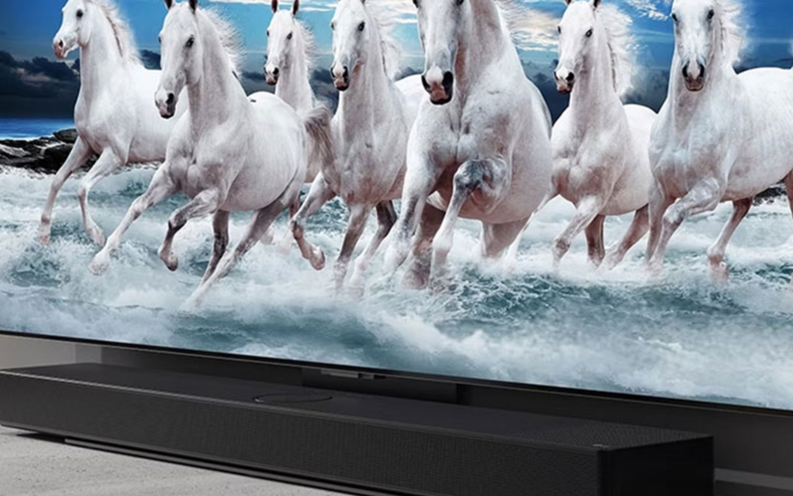 Close-up of a wall-mounted flat-screen TV displaying a dynamic scene of white horses running through water, with a sleek black soundbar placed directly below the TV.