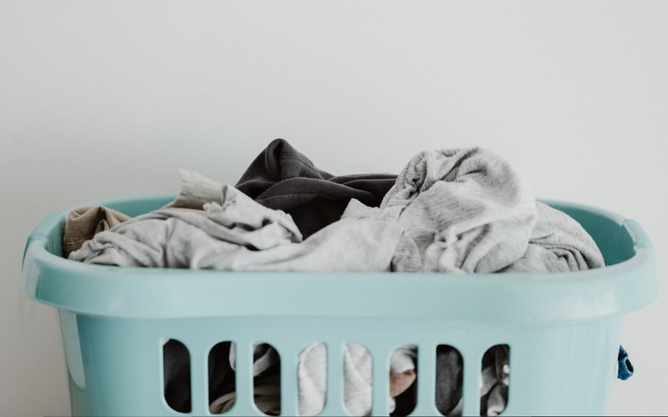  A light blue laundry basket filled with assorted clothes against a plain white background.