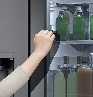 The front view of a black glass InstaView refrigerator with the light on inside. Hands tapping on InstaView screen.