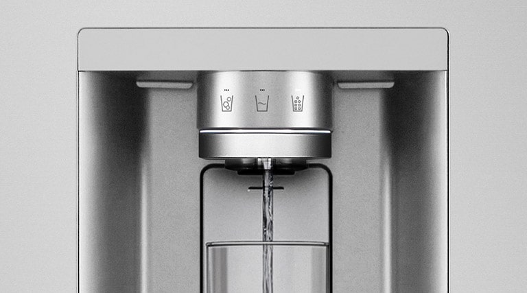 A video starts zoomed in on the water dispenser. The exterior of the refrigerator goes clear and now the interior of the door and mechanical parts of the dispenser nozzle can be seen. The video zooms in further to show the water droplets as they fall through the UVnano part of the nozzle which reduces the bacteria. The view zooms back out to see the exterior of the refrigerator again as water is being dispensed into a glass.