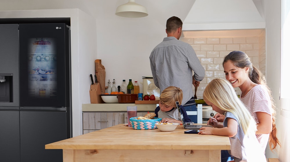 The whole family is sitting at the table preparing a meal. InstaView refrigerator installed on one side of the kitchen is creating cool air quickly.