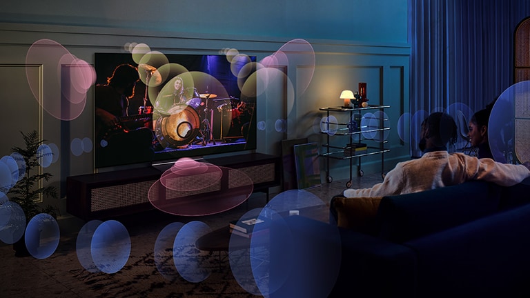 A woman sits on a couch watching a concert with bubbles depicting surround sound around her.